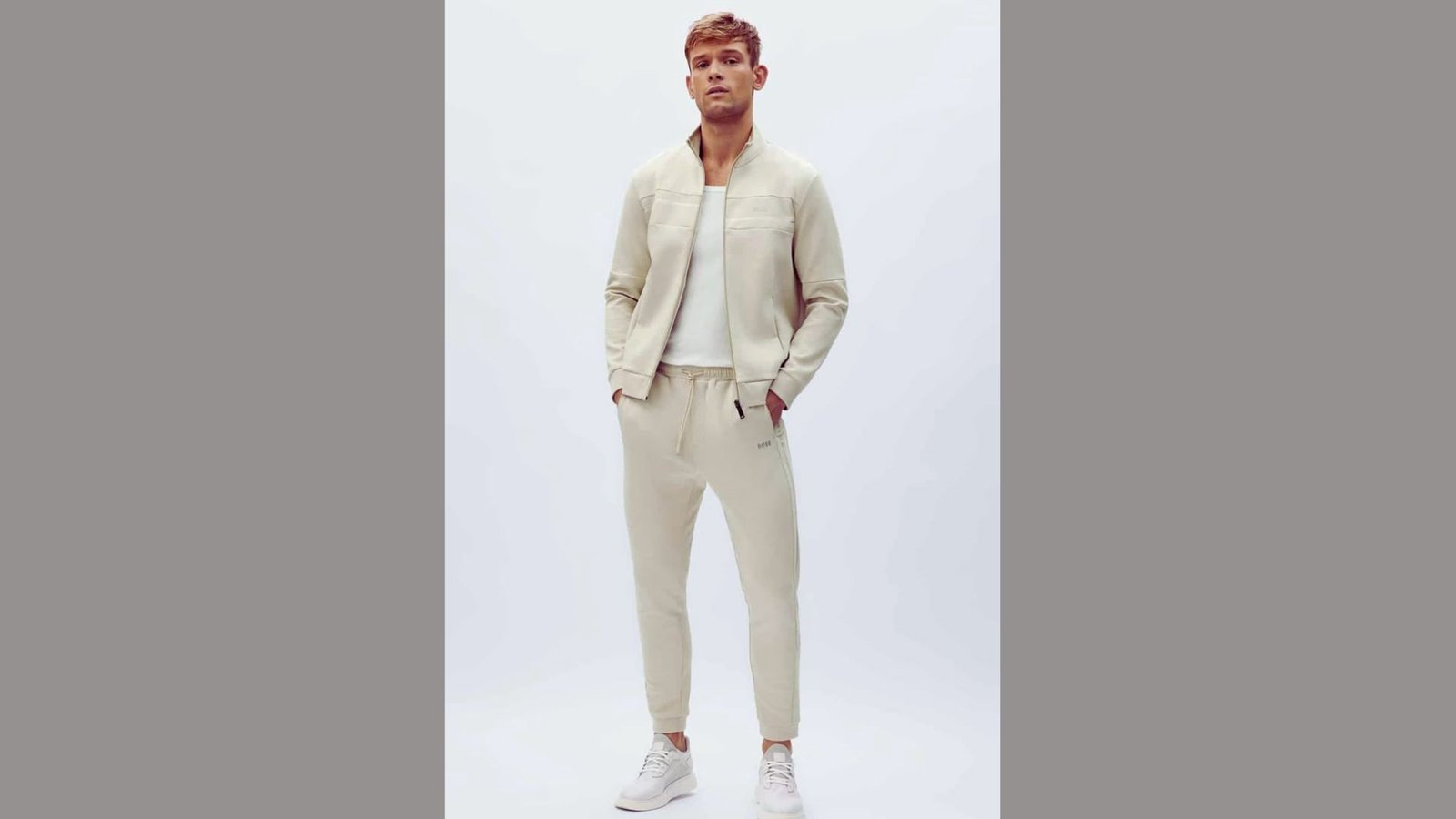 A man wearing a white jacket and white pants stands confidently, showcasing a stylish and modern outfit.