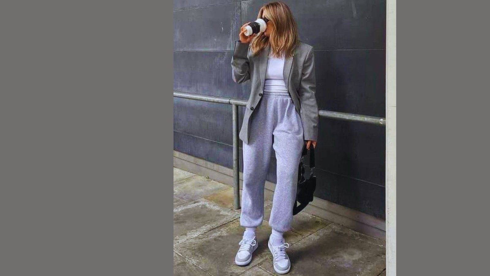 A woman wearing a grey suit paired with white sneakers stands confidently.