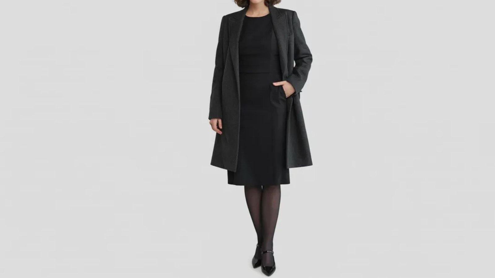 A woman dressed in a black coat over a black dress, exuding sophistication and poise.