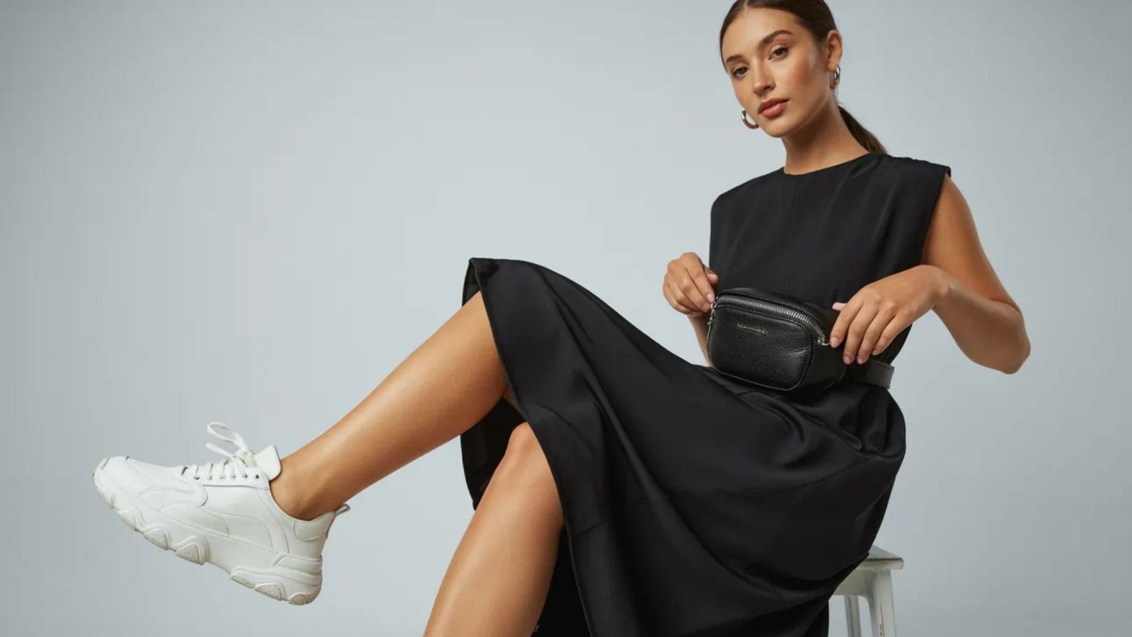 A woman wearing a black dress paired with white sneakers stands confidently, showcasing a stylish and casual look.