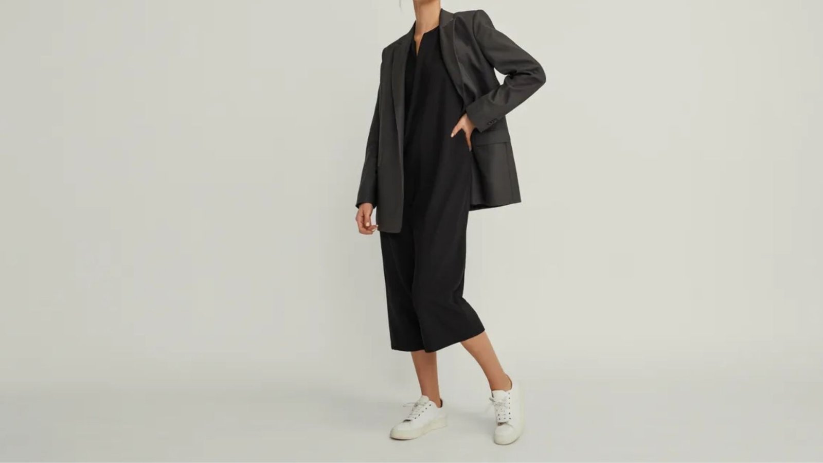 A model dressed in a black suit paired with white sneakers stands confidently, showcasing a modern and stylish look.
