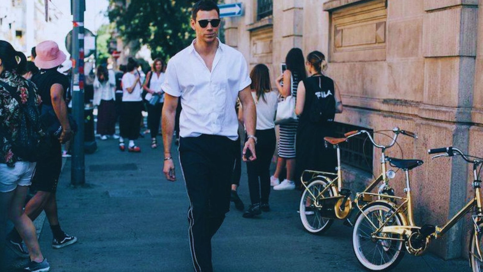 A man wearing a white shirt and sunglasses walks down the street, representing a stylish formal streetwear look