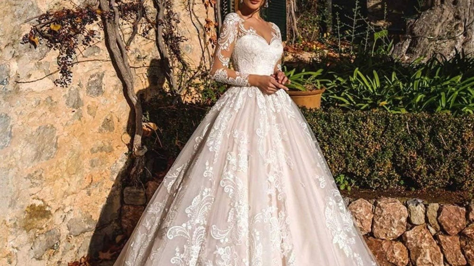 A beautiful woman in a wedding dress stands outside, surrounded by greenery, radiating joy and elegance.