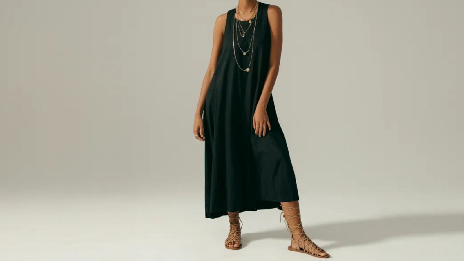 A model displays a chic black dress complemented by elegant sandals.