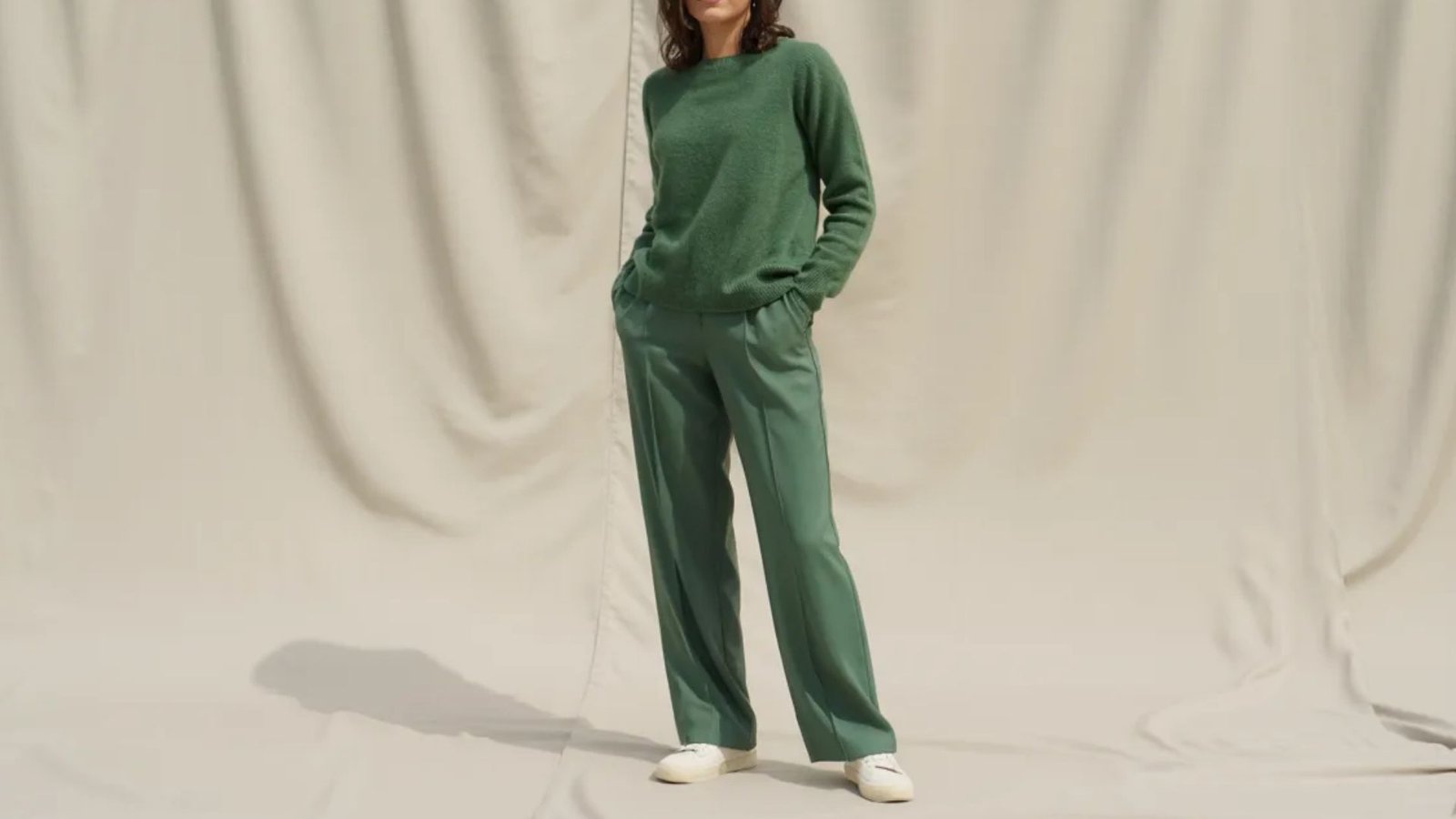 A model showcases a green sweater paired with wide-leg pants, highlighting a stylish and relaxed outfit.
