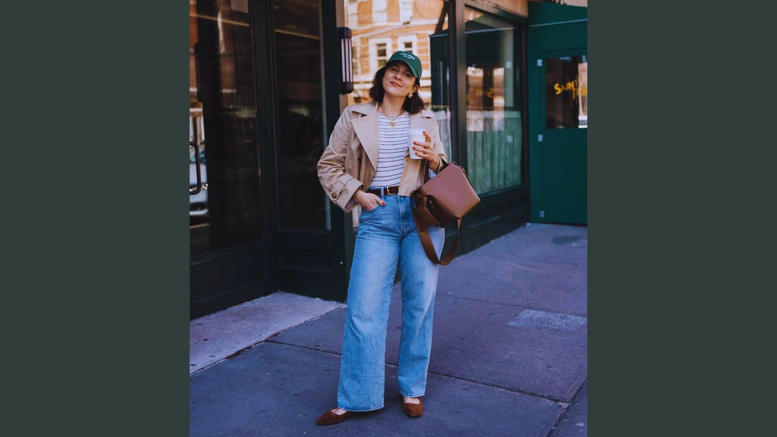  A woman wearing jeans and a jacket stands on the sidewalk, looking confidently ahead.