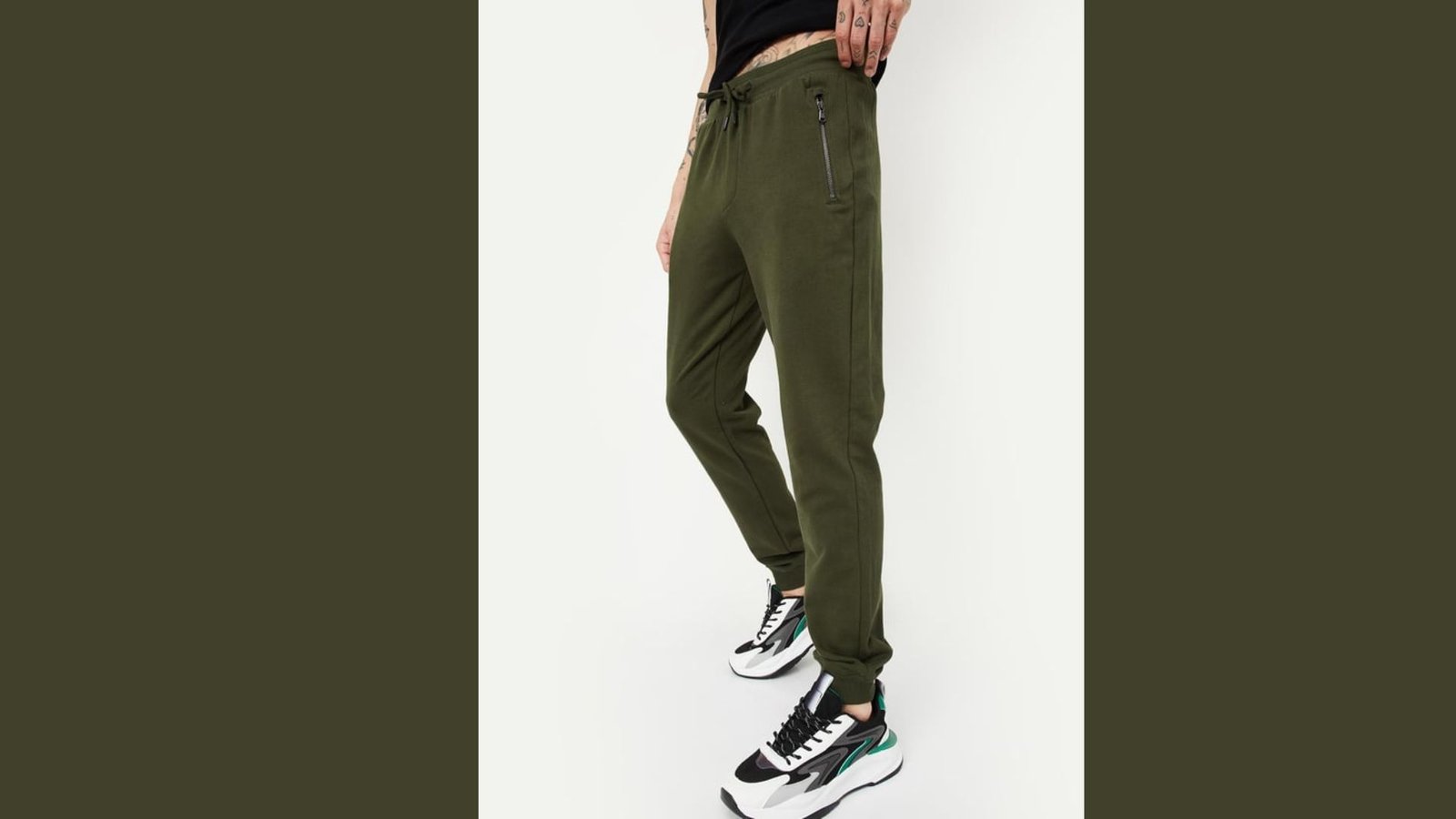 A woman dressed in green sweatpants and sneakers stands confidently, showcasing a casual and sporty outfit.