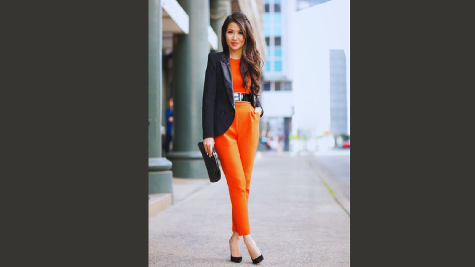 A woman wearing orange pants and a black blazer, styled for a professional office look.
