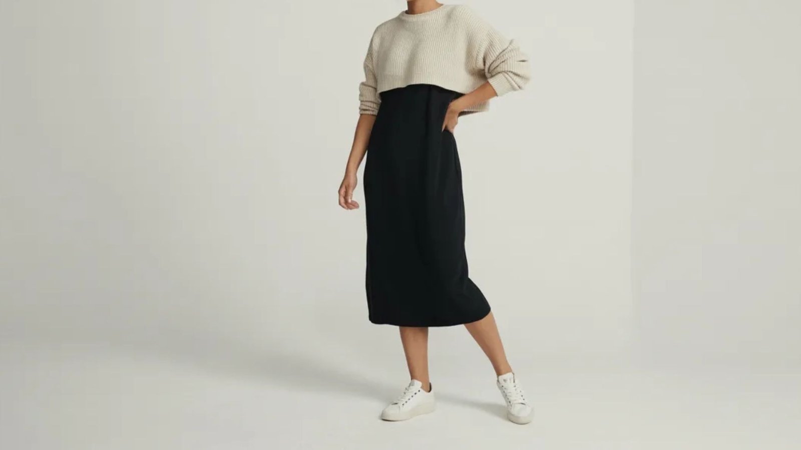 A model showcases a black and white sweater paired with a black midi skirt, highlighting a chic and modern outfit.