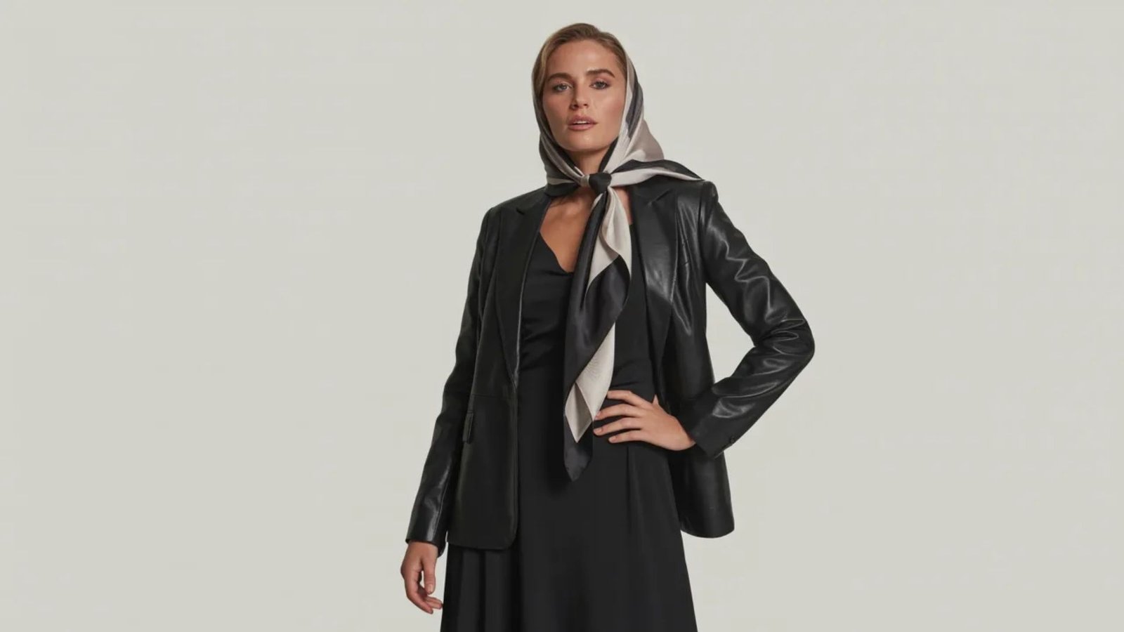 A woman wearing a black dress and jacket stands confidently, showcasing a stylish and elegant look.