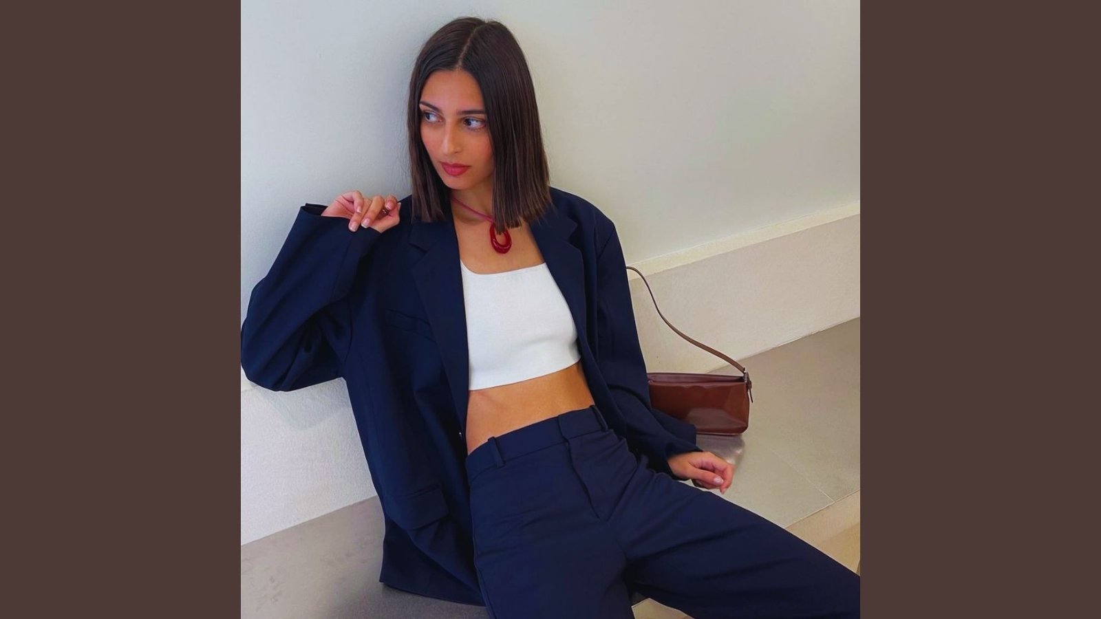 . A woman wearing a white crop top and blue pants stands confidently, showcasing a casual yet stylish outfit.
