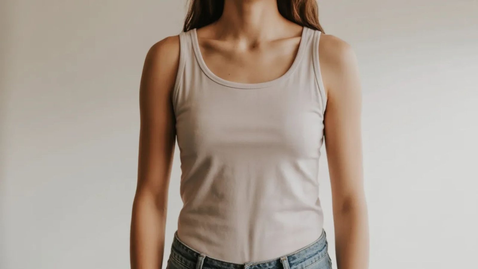 A woman in a tank top and jeans stands confidently, showcasing a casual and stylish outfit.