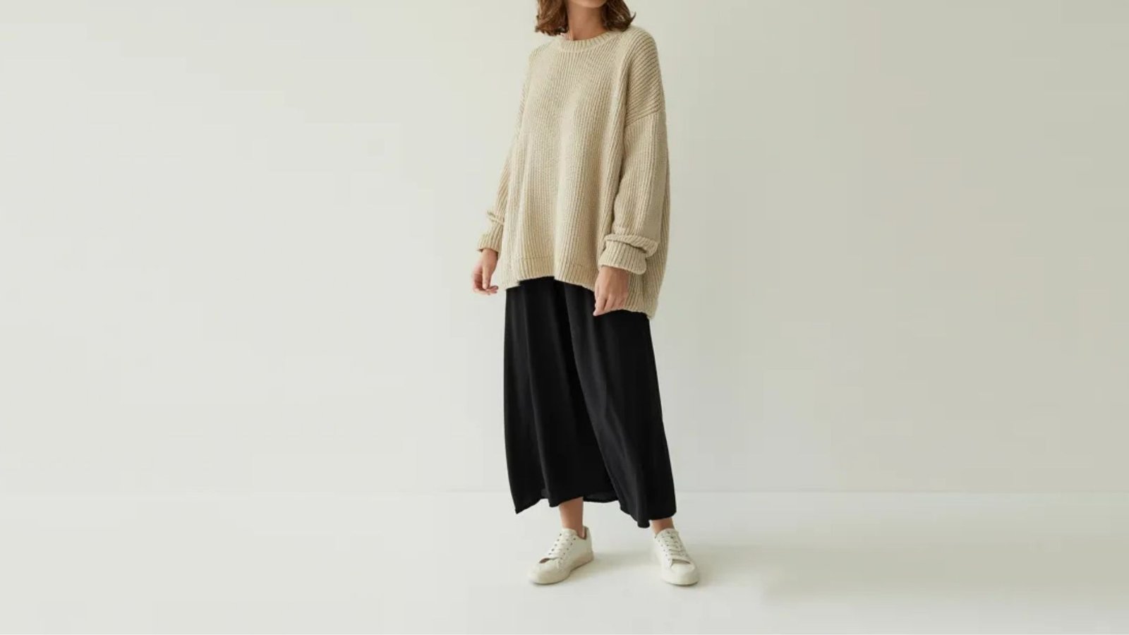 A model showcases a beige sweater paired with wide-legged pants, highlighting a relaxed and stylish outfit.