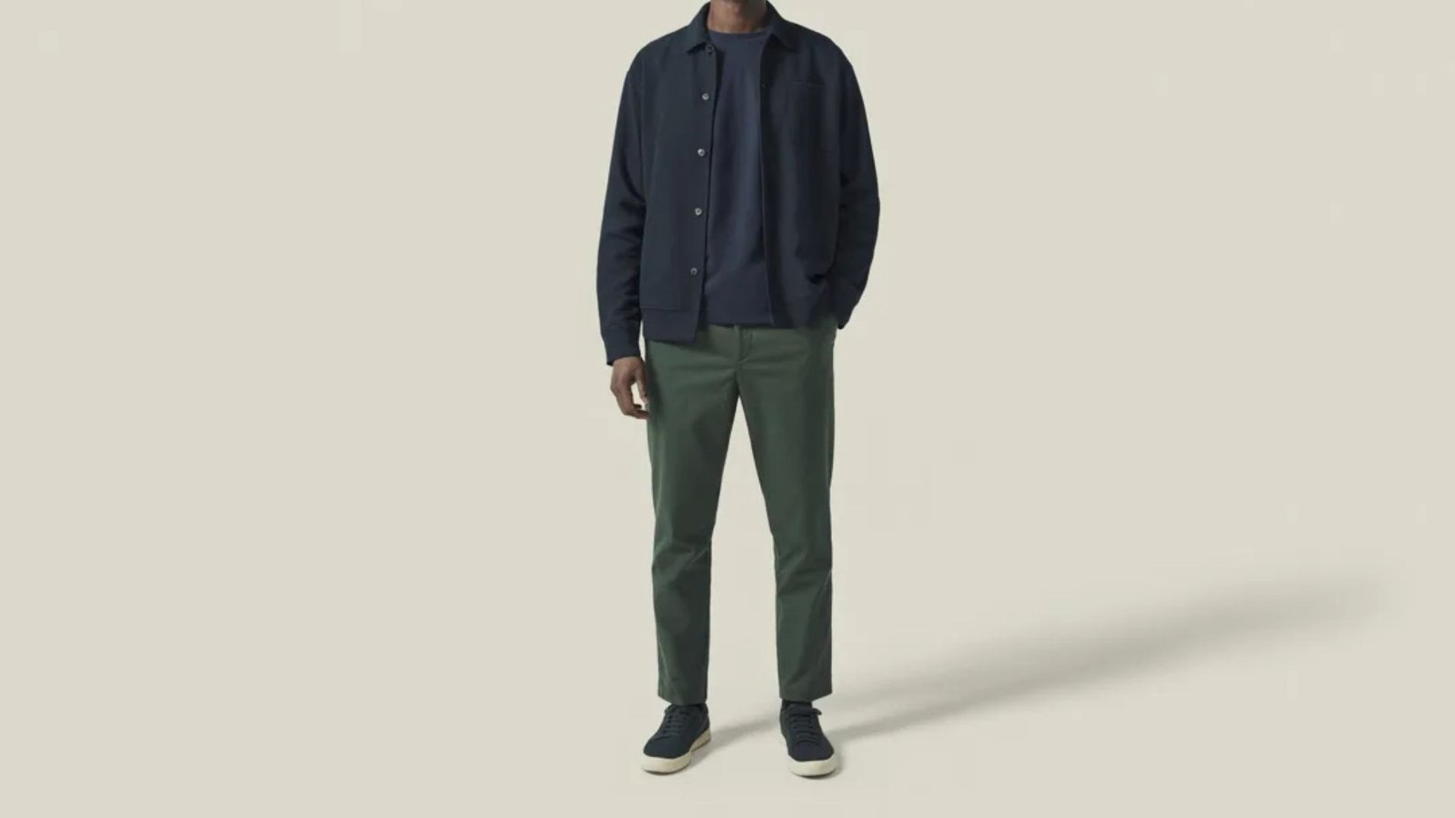 A man dressed in a green shirt and matching green pants poses, highlighting a coordinated and casual look.