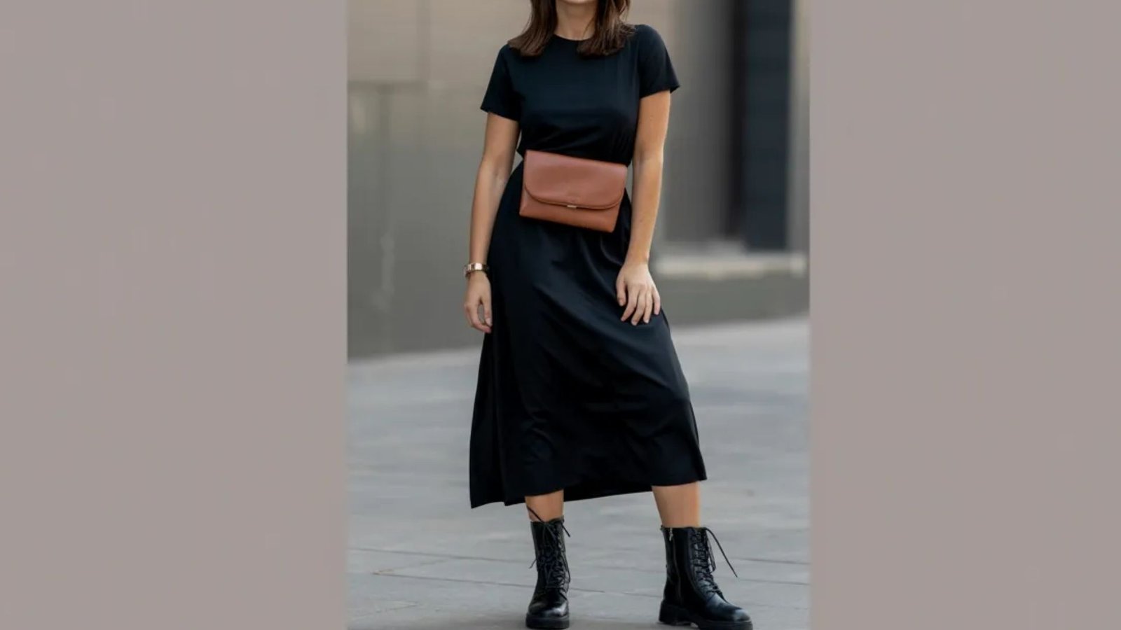 A woman wearing a black dress and boots stands confidently, showcasing her stylish outfit.