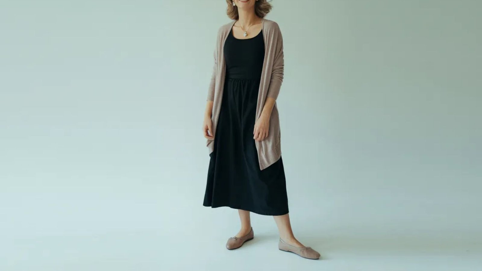 A woman wearing a black dress and cardigan stands confidently, showcasing her elegant style.