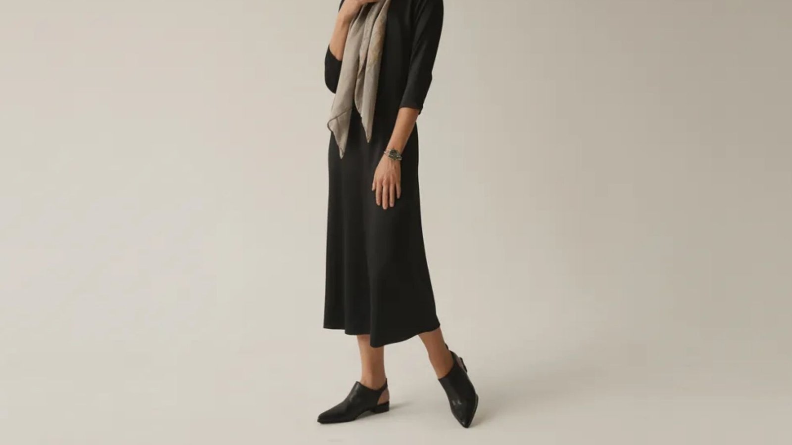 A model showcases a stylish black dress paired with a matching scarf, exuding elegance and sophistication.