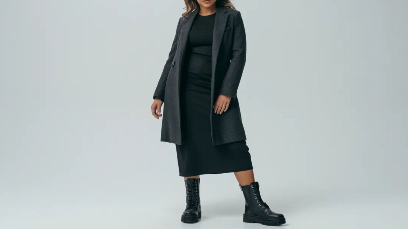 A model showcases a stylish black coat over a matching black dress, exuding elegance and sophistication.