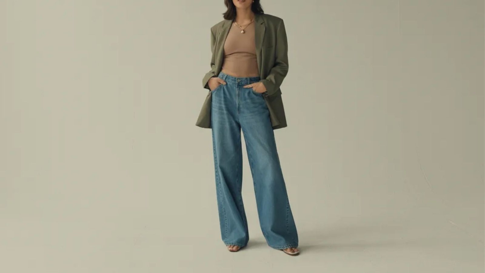A woman wearing a tan top and blue jeans stands confidently, showcasing a casual yet stylish outfit.