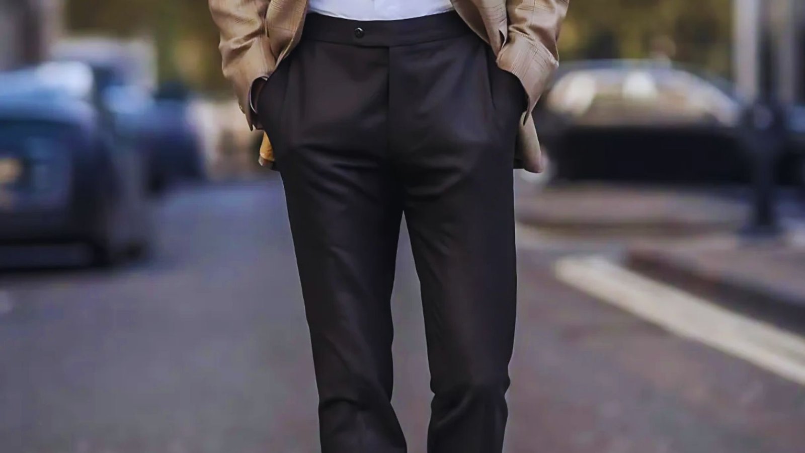 A well-dressed man in a suit and tie stands on a busy street, with shops and cars visible in the background.