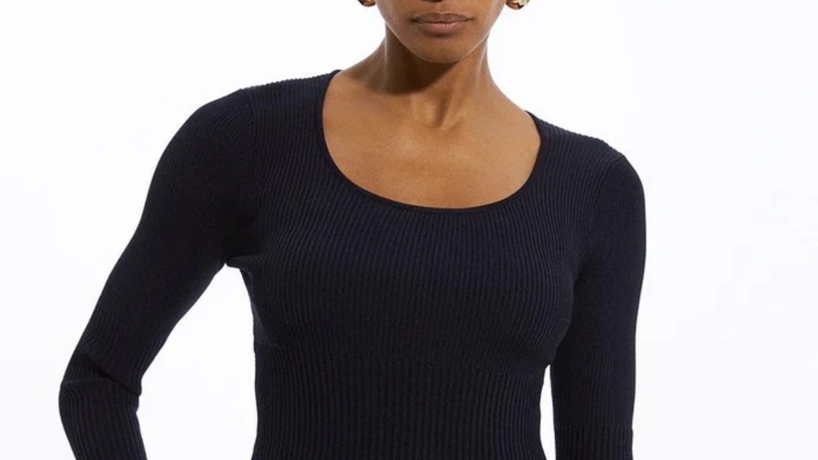 A woman in a black sweater and jeans stands confidently, showcasing a casual yet stylish outfit.