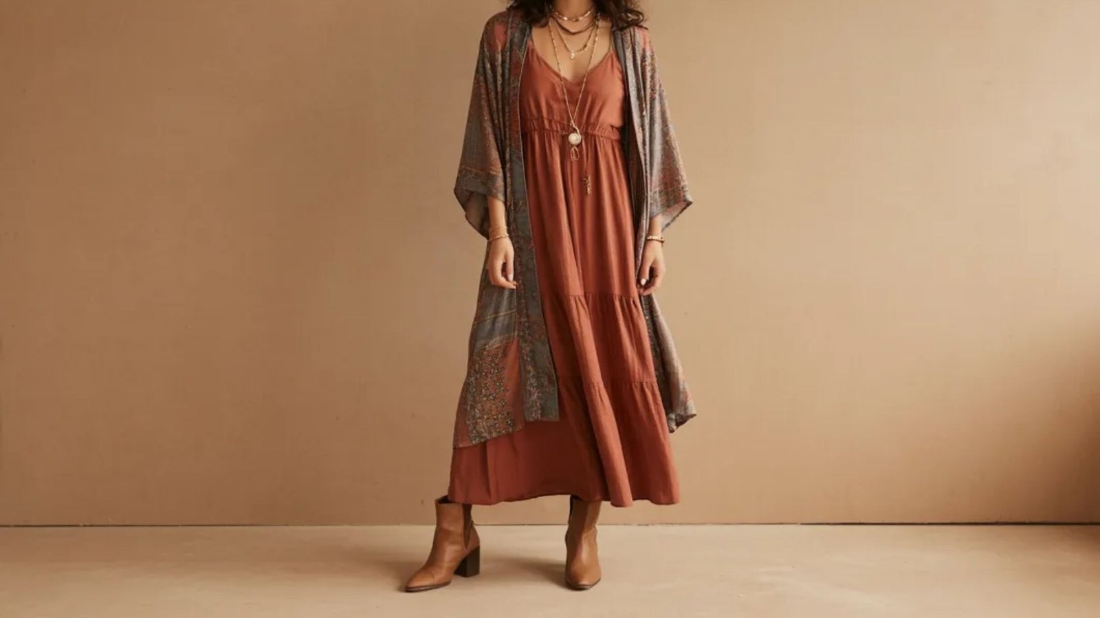 A model showcases a long dress paired with a cardigan and stylish boots, highlighting a chic autumn outfit.