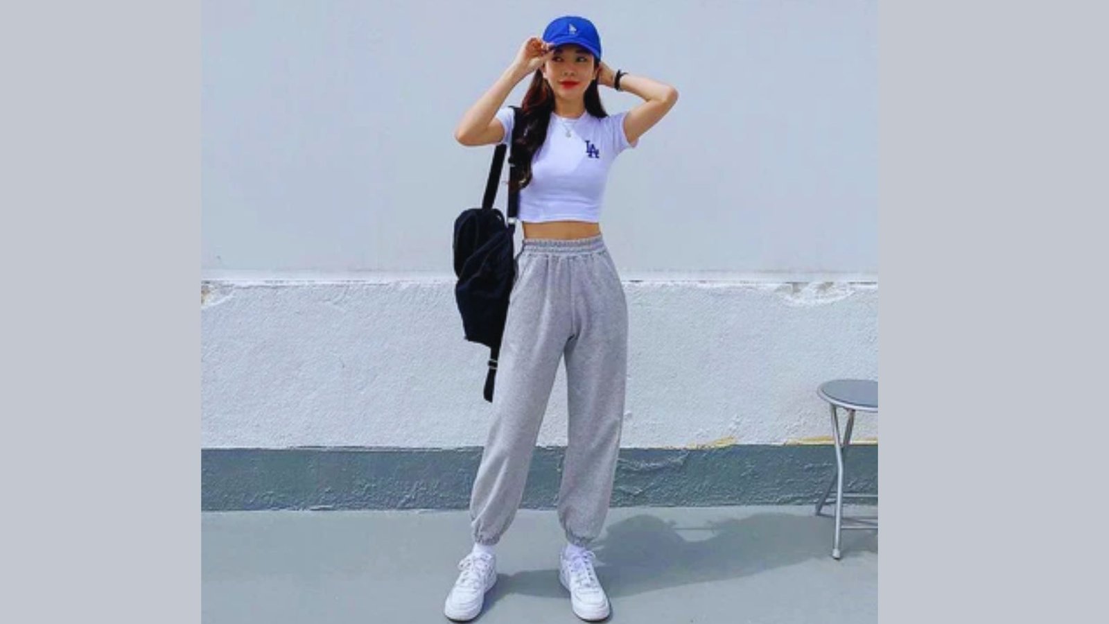 A woman in a white top and grey sweatpants stands confidently, showcasing a casual and comfortable outfit.