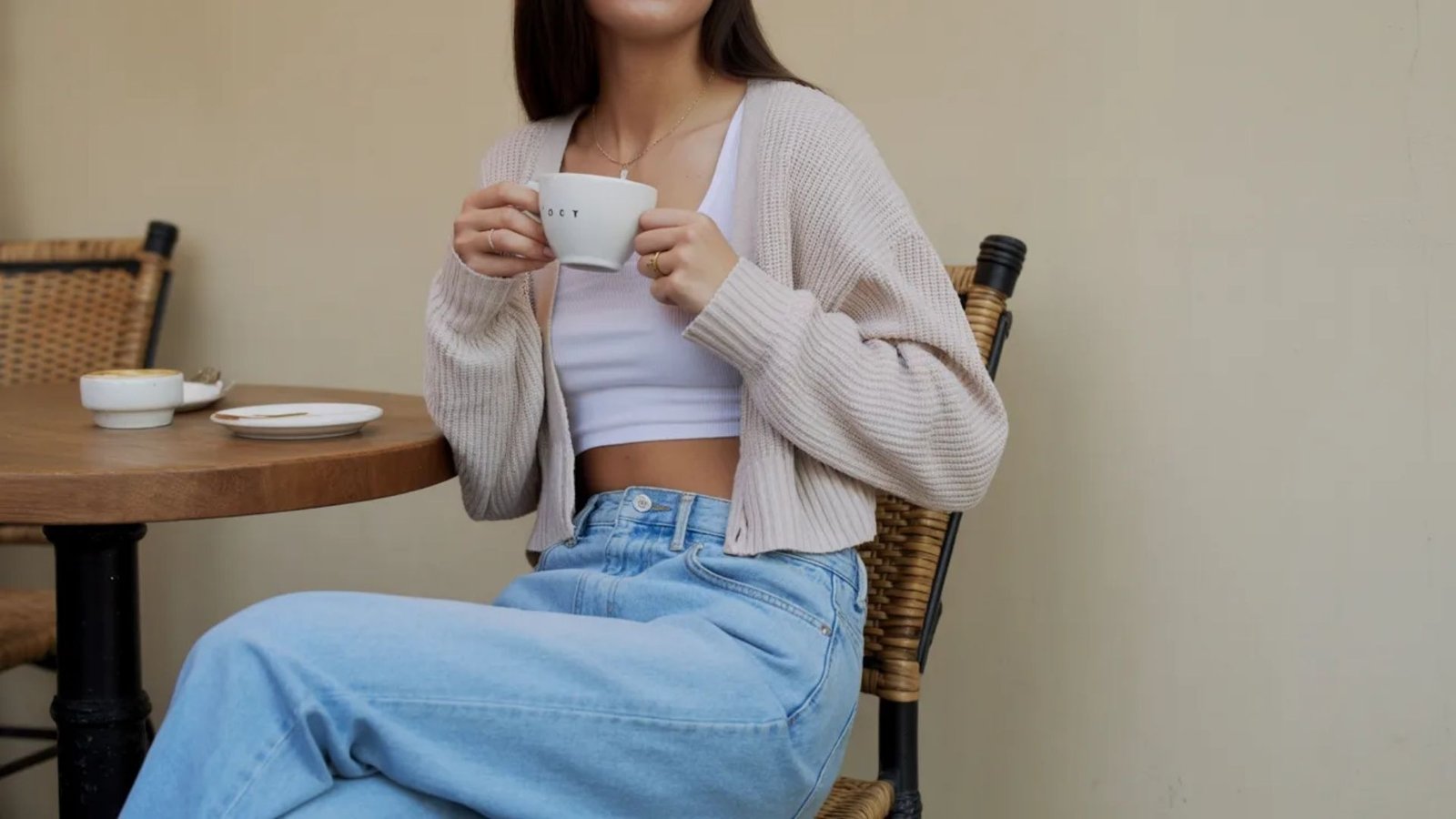 A woman seated at a table, holding a cup of coffee, appearing contemplative.
