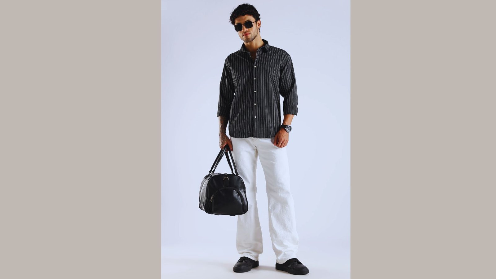A man wearing a black shirt and white pants stands confidently, showcasing a stylish and modern outfit.
