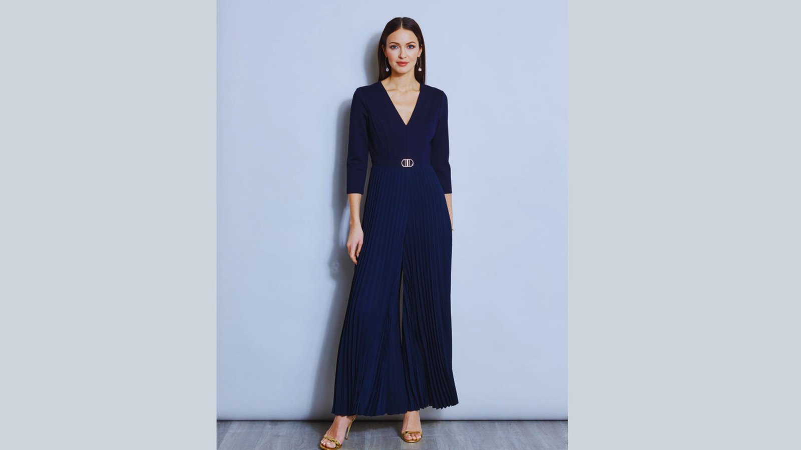 A model showcases a fitted navy jumpsuit with a belt, complemented by a stylish peacoat.
