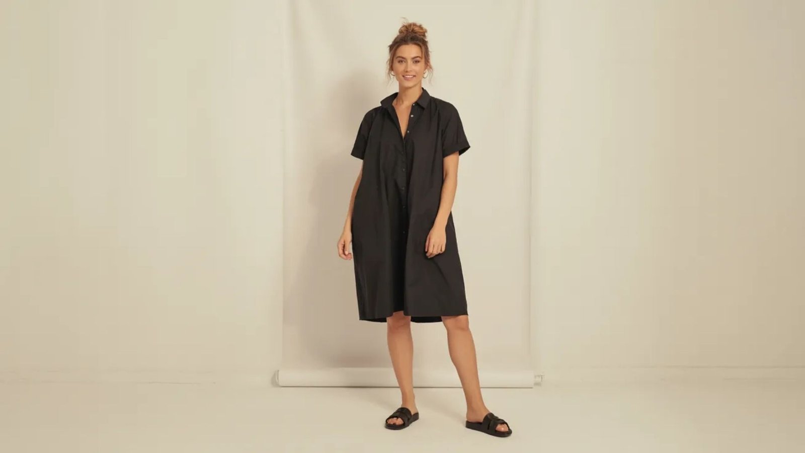 A model wears a chic black shirt dress and comfortable sandals.