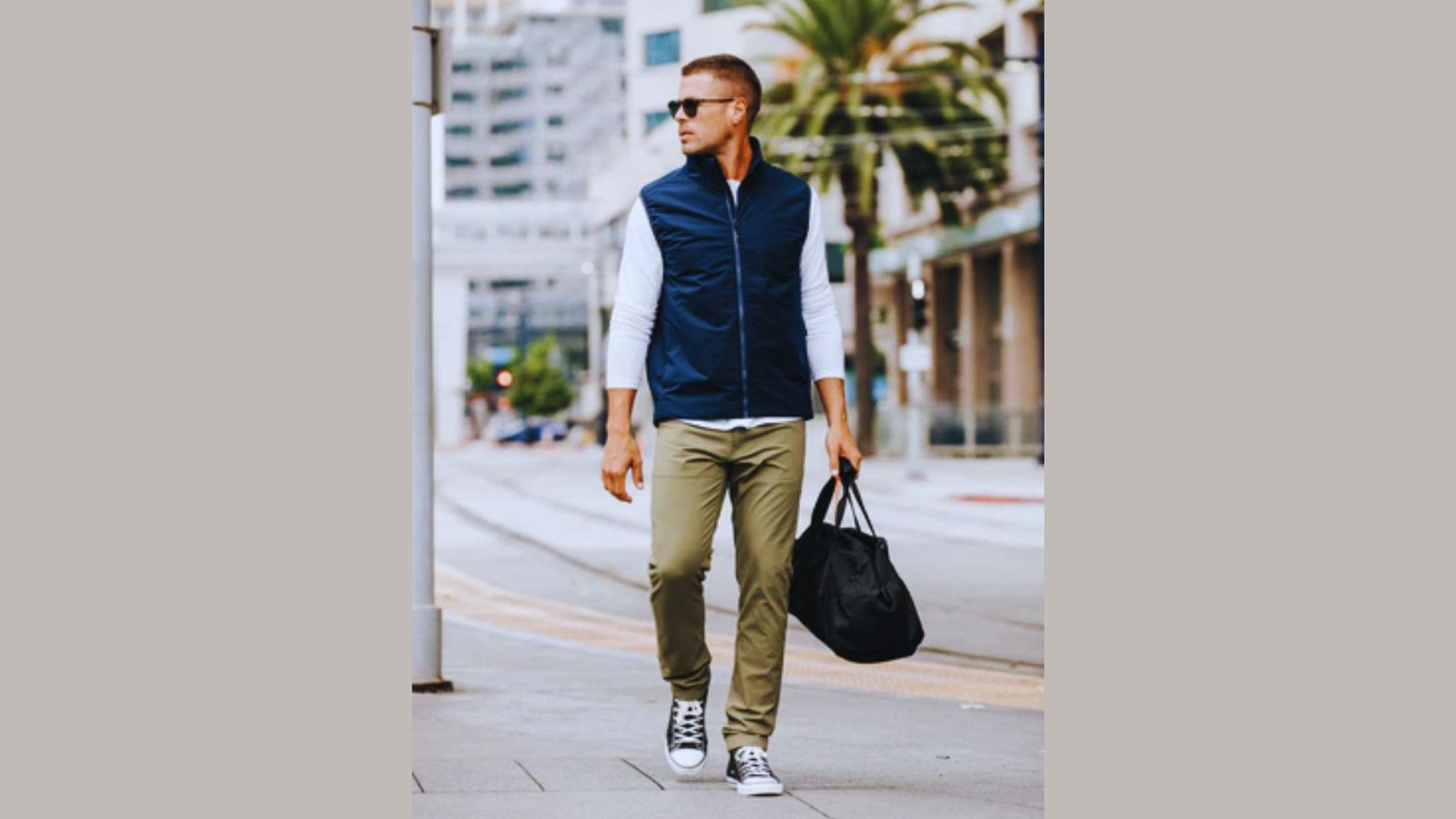 A man wearing a blue vest and khaki pants walks down the street, surrounded by urban scenery.