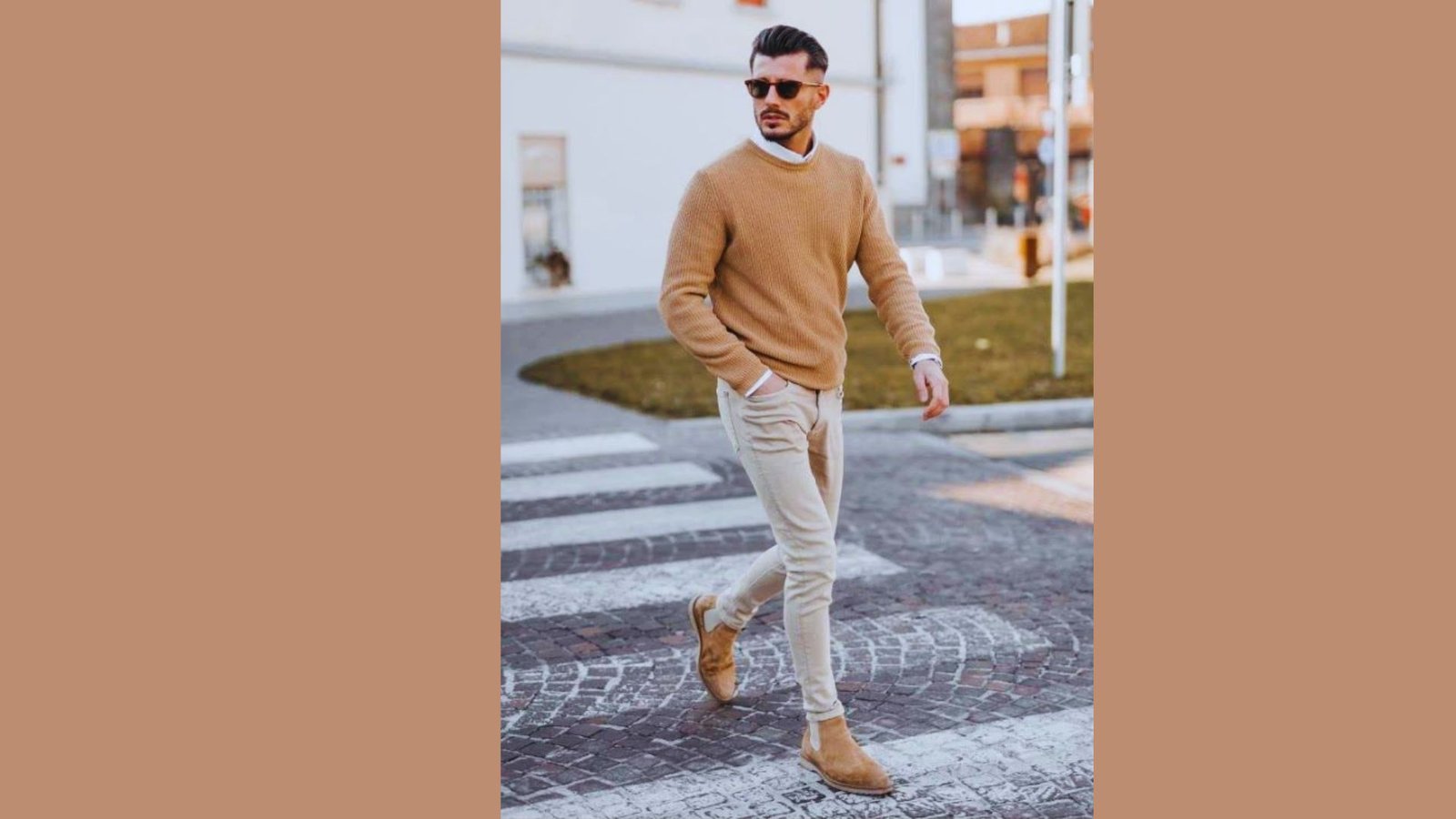 A man wearing a tan sweater and jeans is crossing the street.