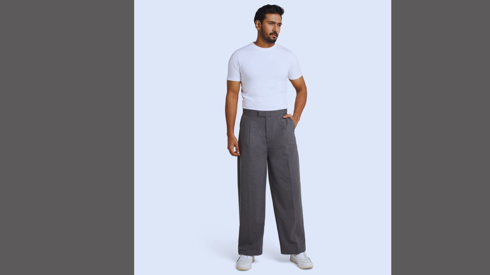 A man wearing a white t-shirt and grey pants stands confidently, showcasing a casual and relaxed style.