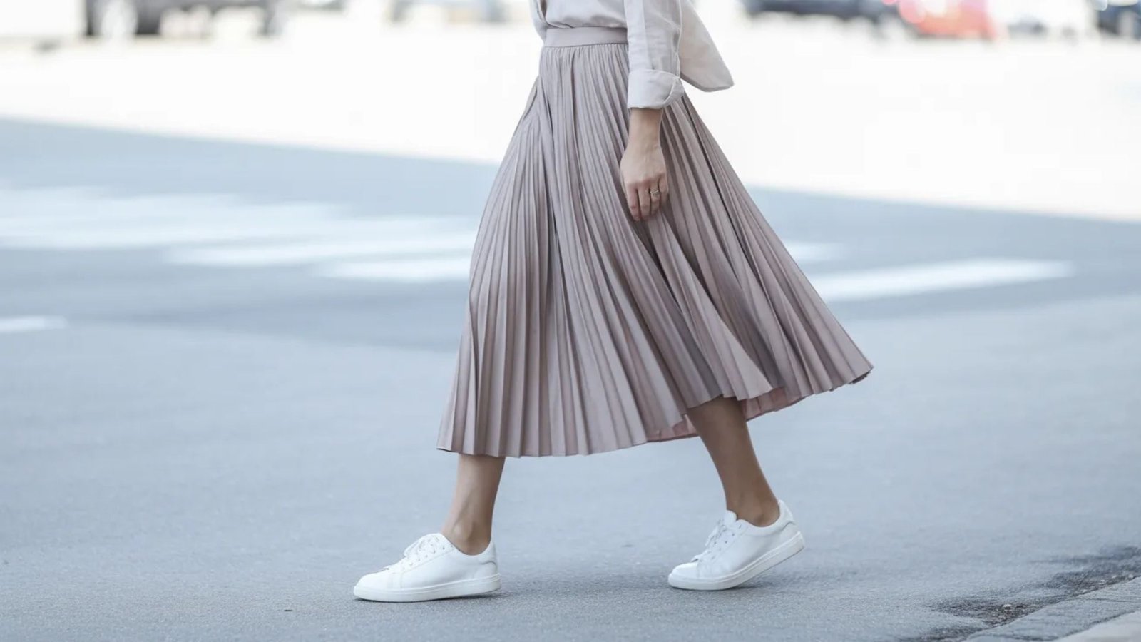 A woman in a pleated skirt and white sneakers stands confidently, showcasing a stylish and casual outfit.