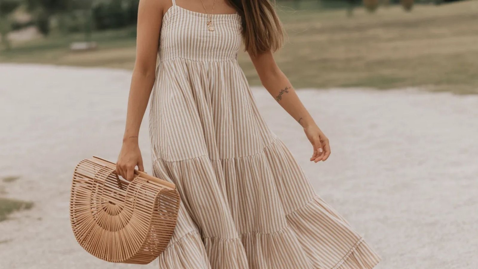 A woman wearing a beige striped dress holds a straw basket, set against a vibrant outdoor scene.