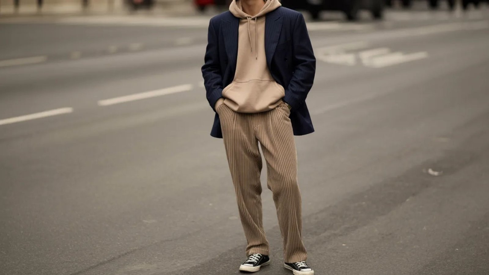 A man in a suit and sneakers stands confidently on a city street, blending formal and casual styles.