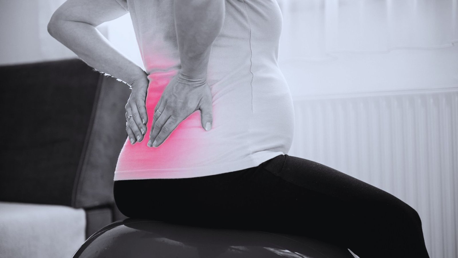A pregnant woman on a ball, showing discomfort from back pain, emphasizing the impact of wearing heels during pregnancy.