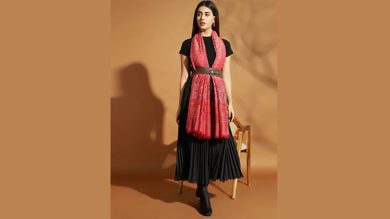 A woman wearing a black dress and a red scarf stands elegantly, showcasing her stylish outfit.