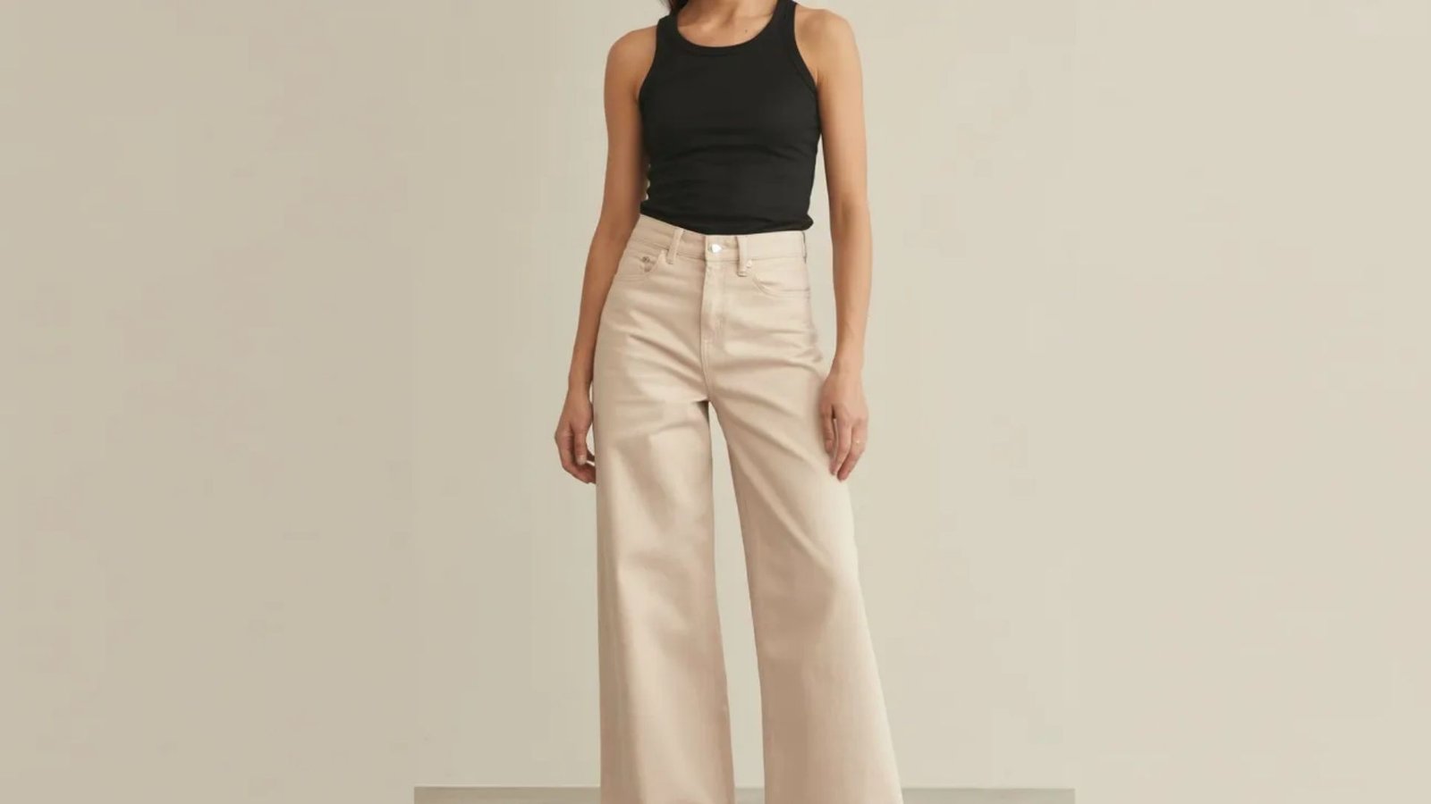 A model showcases a black top paired with beige wide-leg pants, highlighting a stylish and modern outfit.
