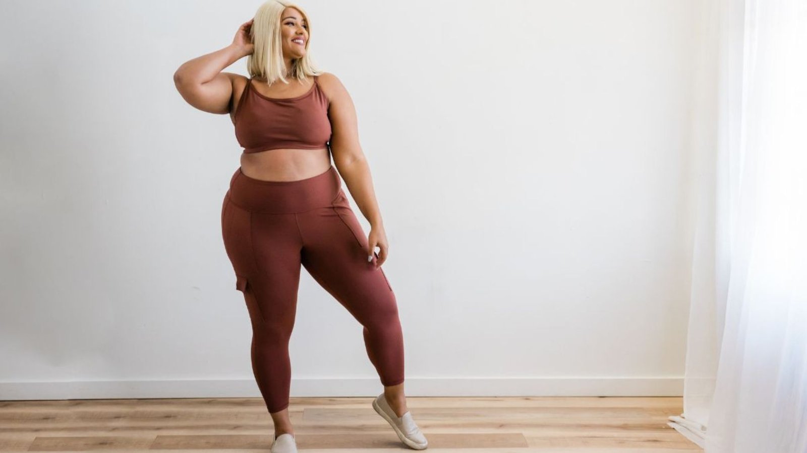 A woman in a brown sports bra and leggings poses confidently, showcasing her athletic wear.
