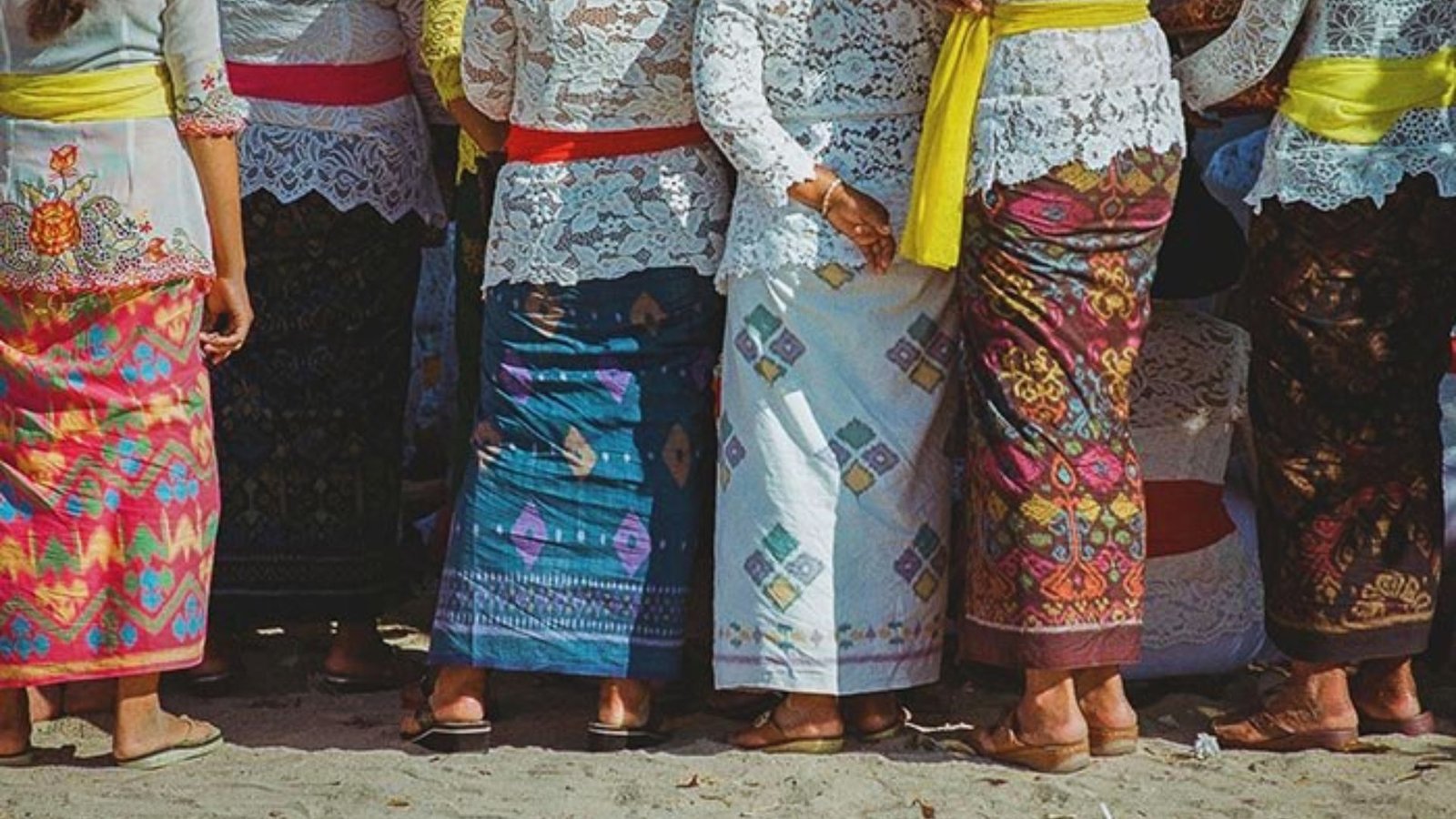  A group of women in vibrant clothing stands together on the beach, enjoying the sunny day and ocean view.
