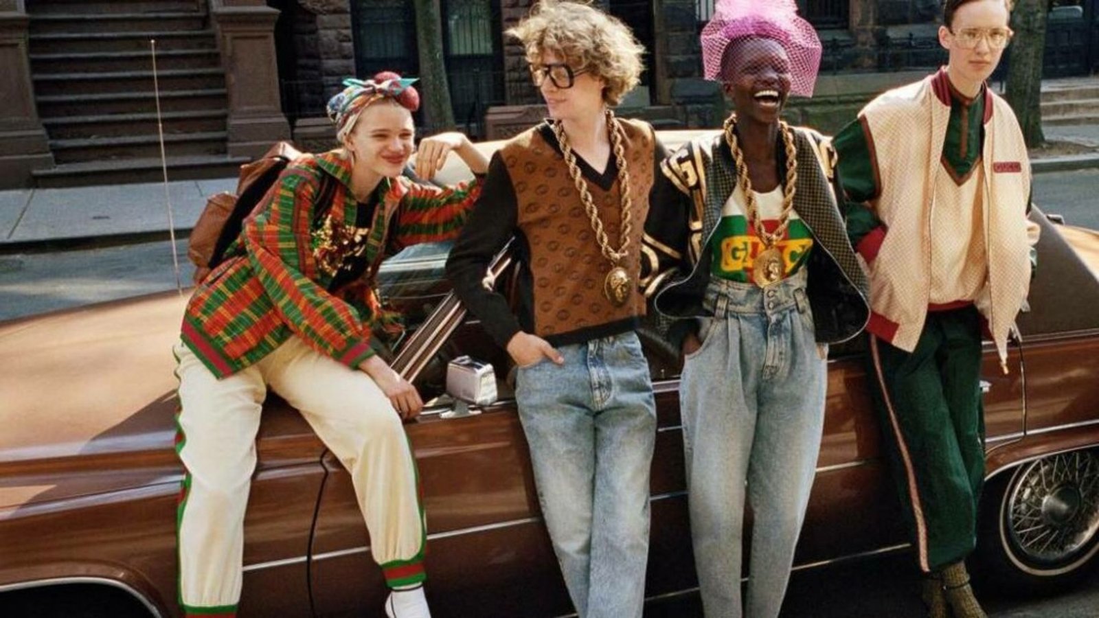Four young friends sitting on the hood of a parked car, engaged in conversation and enjoying a sunny day together