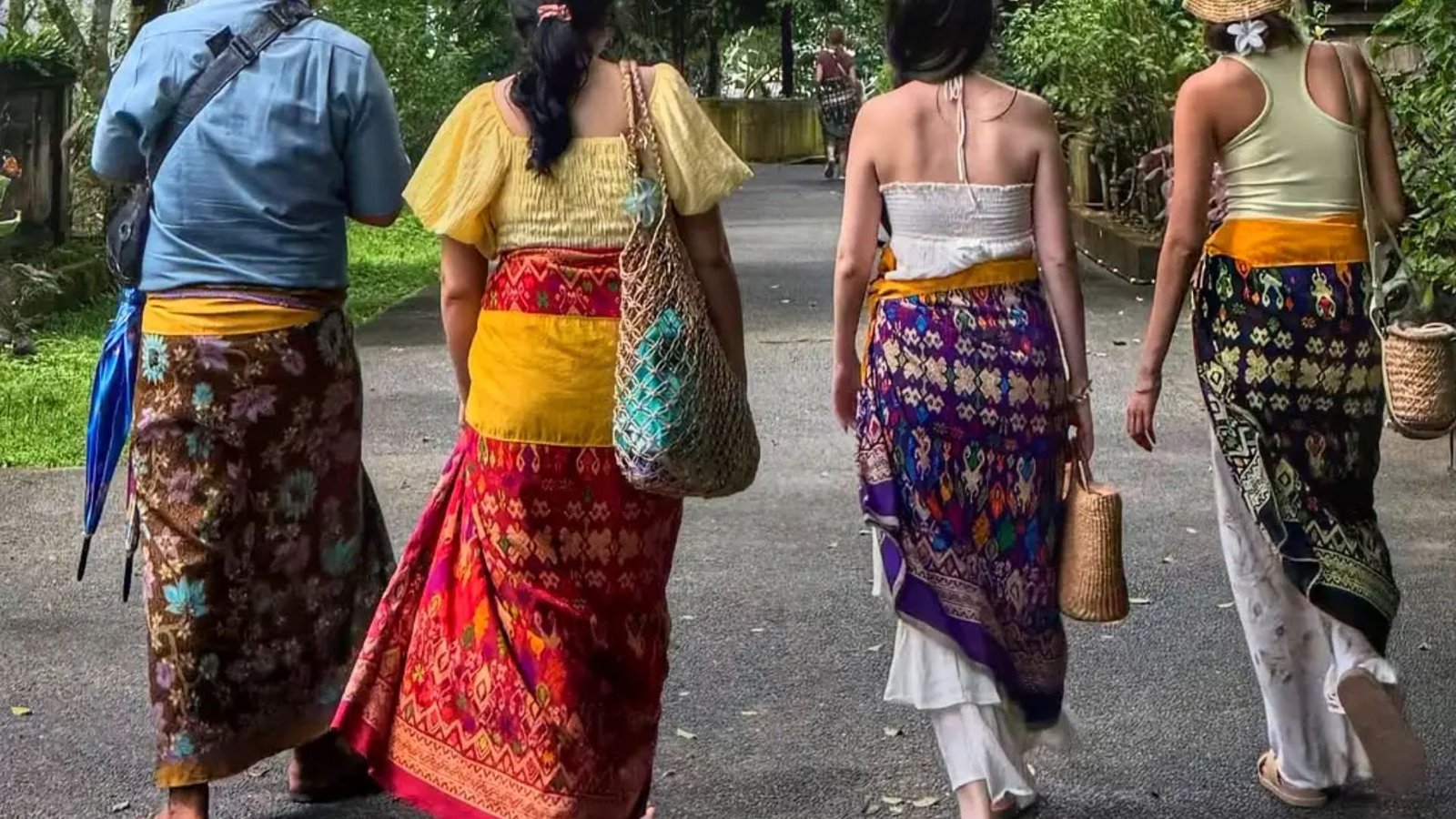 Three women in vibrant skirts stroll along a scenic path, enjoying a sunny day outdoors.