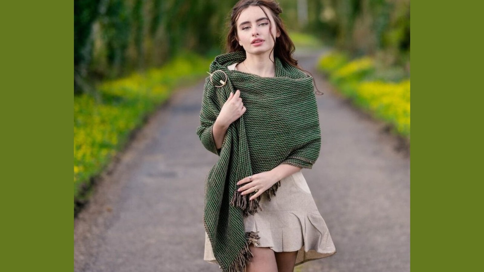 A woman in a green shawl walks along a scenic path surrounded by greenery.