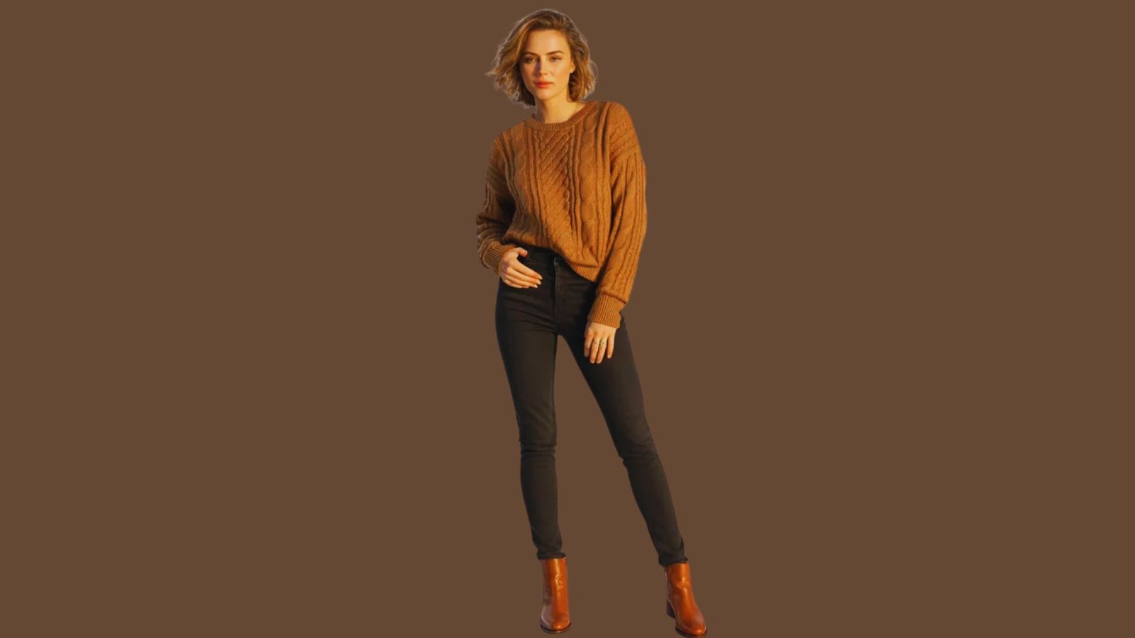 A woman wearing a brown sweater and black pants stands confidently, showcasing a casual yet stylish outfit.