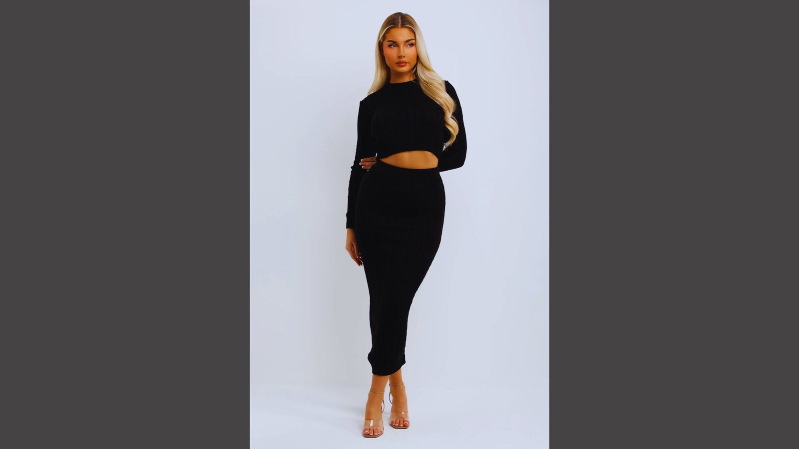 A woman wearing a black dress and heels stands confidently, showcasing her elegant style.