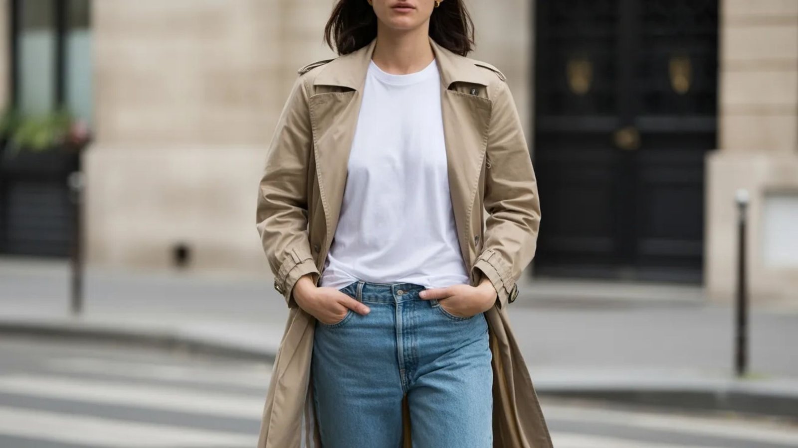 A woman wearing jeans and a trench coat stands confidently, showcasing a stylish and casual outfit.