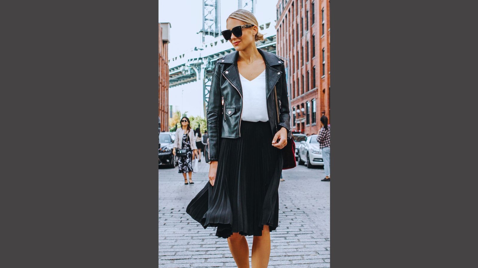 A woman wearing a black skirt and a leather jacket stands confidently, showcasing a stylish and edgy look.