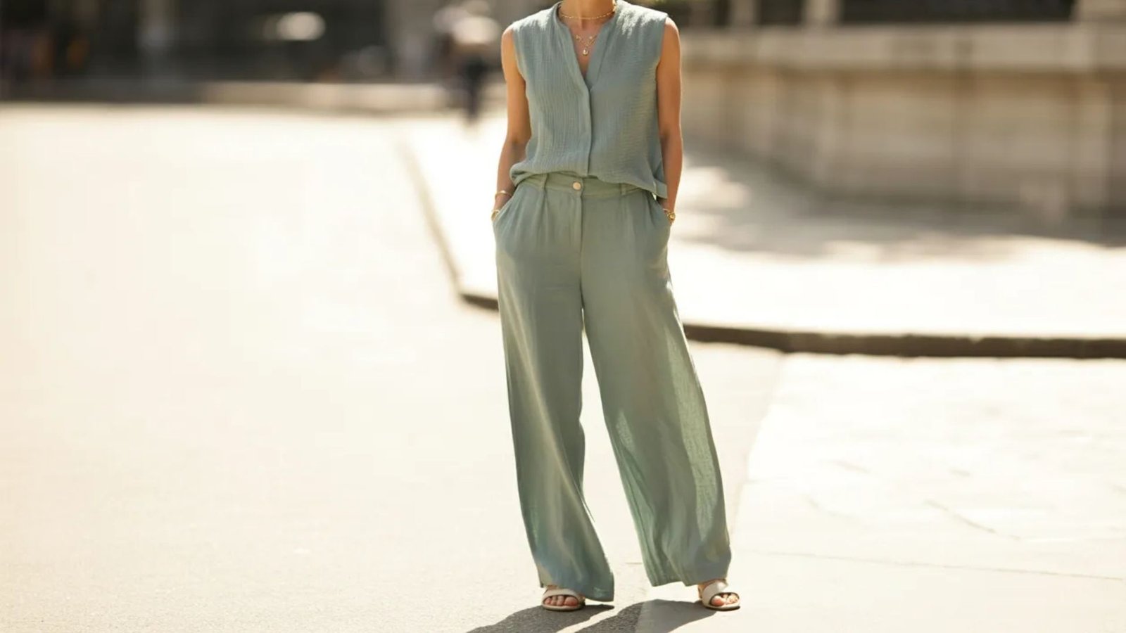 A woman wearing a green jumpsuit and sandals stands confidently, showcasing a stylish and casual summer outfit.